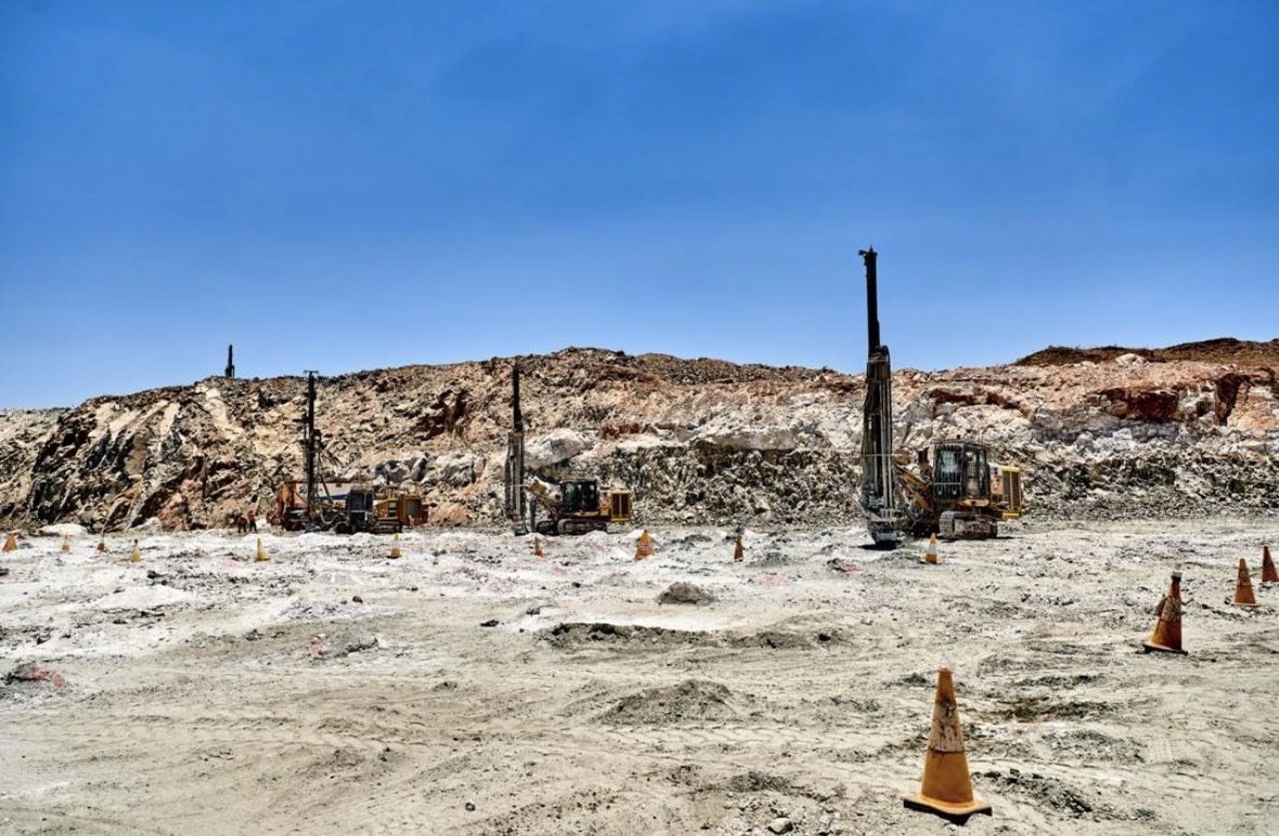 Track-mounted blast hole rigs drilling a marked pattern on an open-pit bench